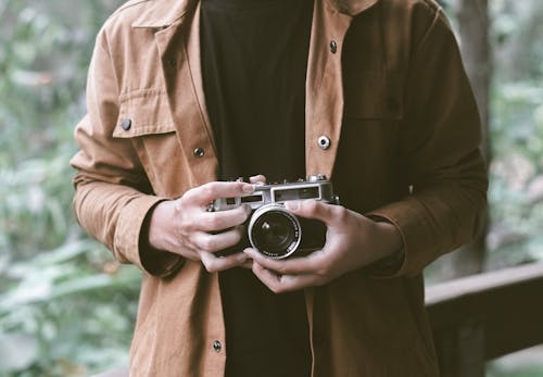 Kostnadsfri bild av analog kamera, brun jacka, håller