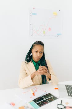 Professional woman with braided hair analyzing finance charts in a modern office setting.