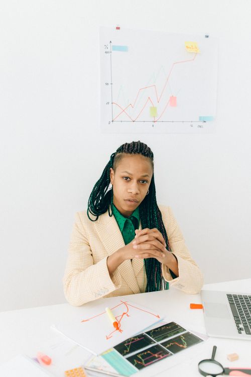 Free Professional woman with braided hair analyzing finance charts in a modern office setting. Stock Photo