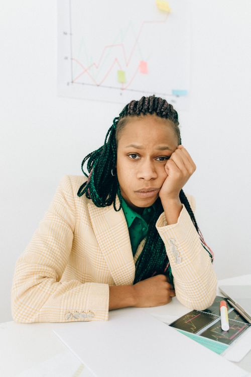 Free African-American woman with braided hair in a blazer, looking bored in an office. Stock Photo