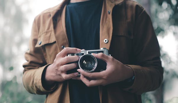 A person in a brown jacket holding an analog camera, outdoors in East Java, Indonesia.