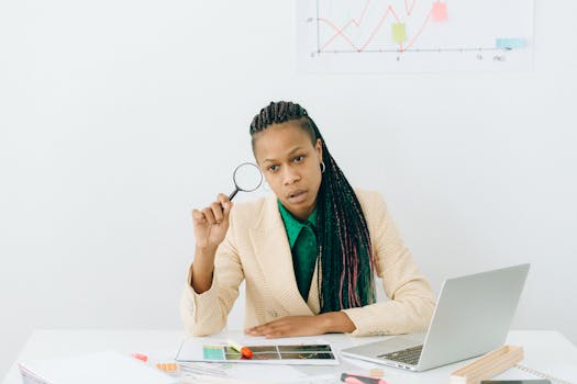 An attentive woman using a magnifying glass to examine documents in an office setting.