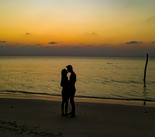Free Silhouette of a couple sharing a romantic moment on a tranquil beach at sunset. Stock Photo