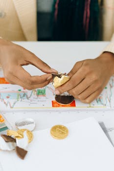 Close-up of hands unwrapping gold chocolate coins on a financial chart, symbolizing investment concepts.
