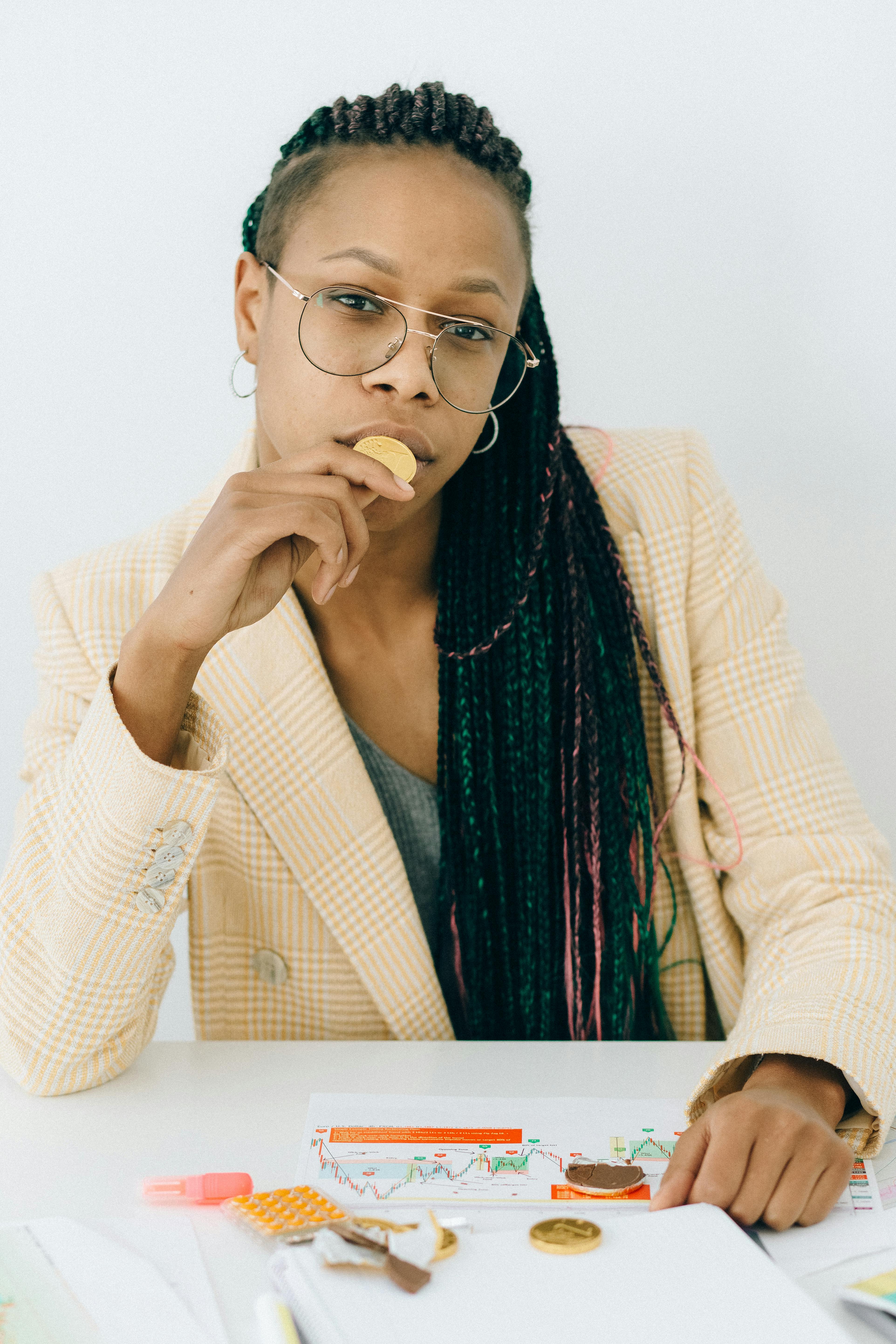 woman in a beige coat holding a gold chocolate coin while sitting by the table