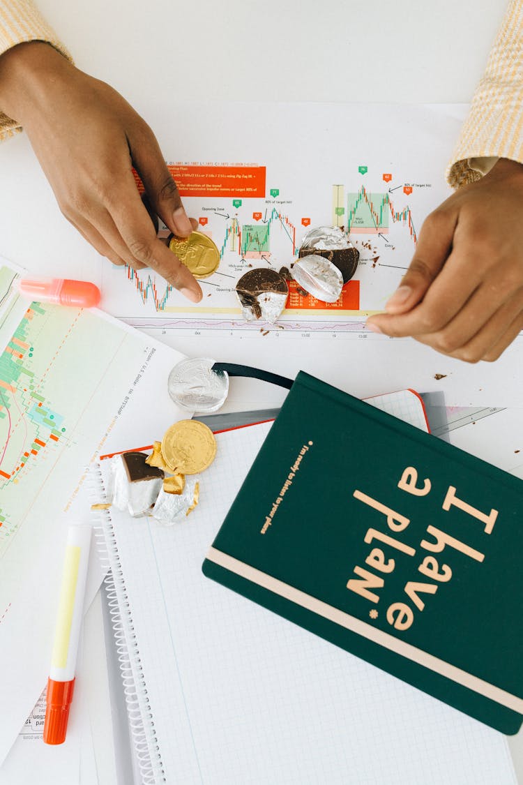 Person Holding A Gold Chocolate Coin On The Table With A Green Book