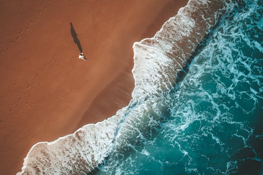 Stunning aerial photo of a man walking along a sandy beach in Chukai, Malaysia, with crashing waves.