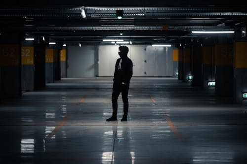 Man in Black Hoodie and Pants Standing on Gray Concrete Floor of a Carpark