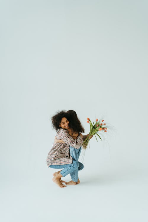 Free A Woman in Blue Denim Jeans Hugging Her Daughter while Holding Flowers Stock Photo