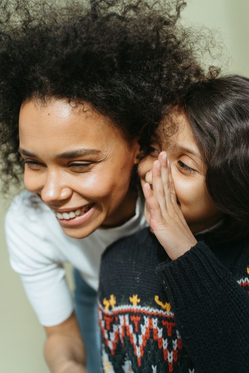 Free Mother and daughter share a joyful moment of whispering and laughter indoors. Stock Photo