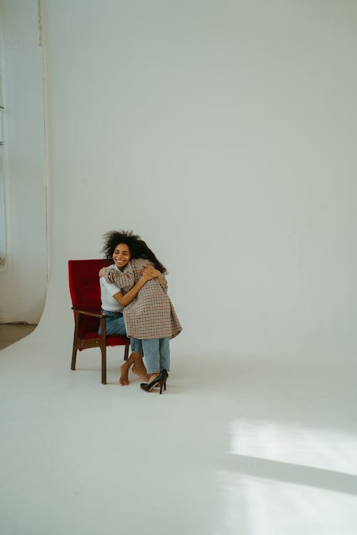 Woman Hugging a Child while Sitting on a Chair