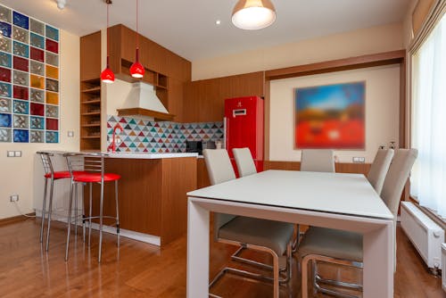 Interior of stylish kitchen zone with bright furniture and tile placed near dinning table in modern apartment