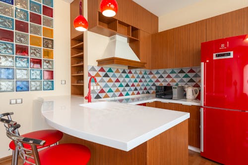 Interior of empty stylish kitchen zone with red fridge and colorful walls in apartment in daytime