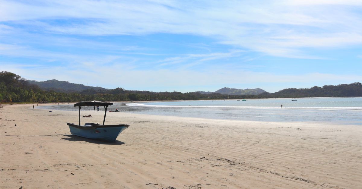 Tranquil beach scene at Sámara, Costa Rica, featuring a lone boat on sandy shores under a blue sky.