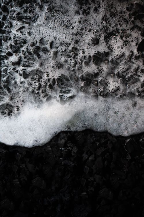 Free Dramatic close-up of waves splashing over dark stones, showcasing texture and contrast. Stock Photo