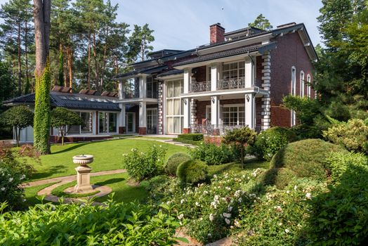 Green grass and trees on meadow in yard near cottage facade in sunny summer day