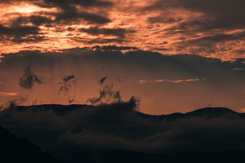 Free A stunning sunset with sun rays piercing through dramatic clouds over a silhouetted mountain range. Stock Photo