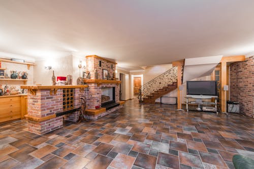 Interior of spacious empty mansion with counter near cabinet next to fireplace and TV near stairway