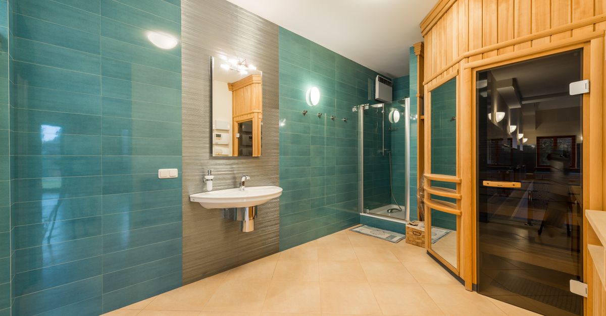 Interior of light shower room with glass cabin and sink and wooden entrance to sauna room with glass doorway