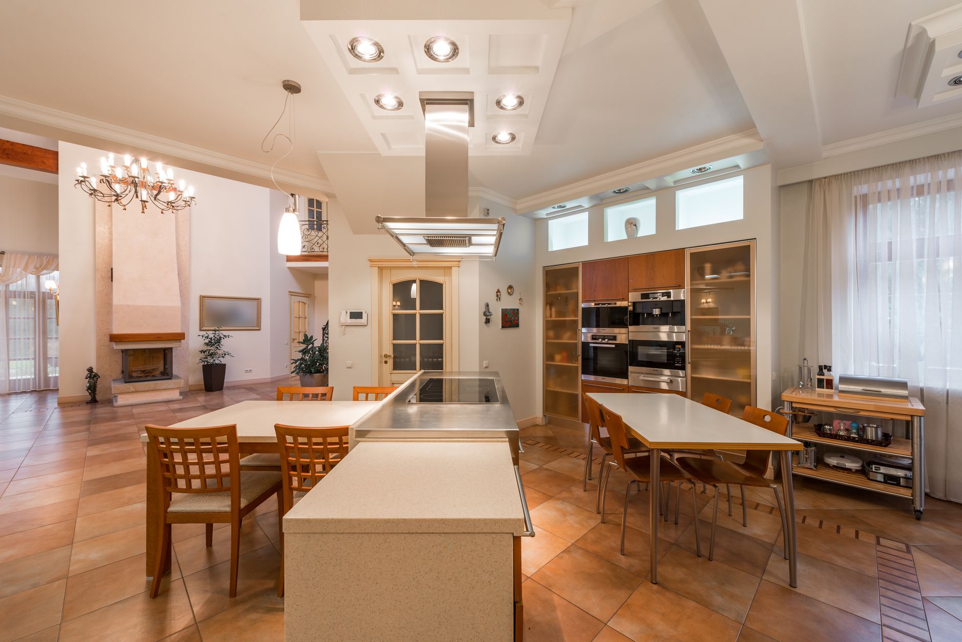 Interior of dining area of modern spacious open plan kitchen with wooden furniture and illuminated lamps on ceiling