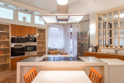 Free Interior of contemporary kitchen with wooden cabinets and built in appliances and island counter with stove top illuminated with bright lamps Stock Photo