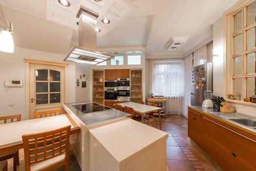 Spacious light modern kitchen with white and brown furniture and built in appliances in daytime