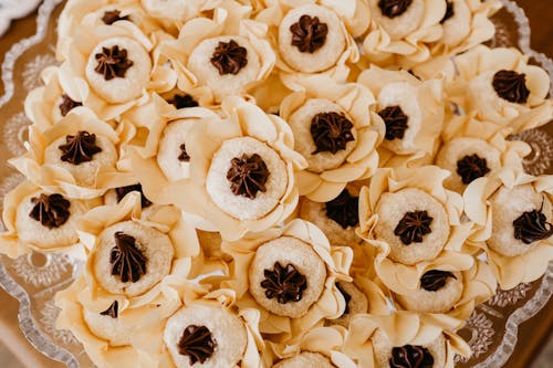 Top view of tasty round shaped biscuits with chocolate cream in decorative flowers on transparent plate during festive event