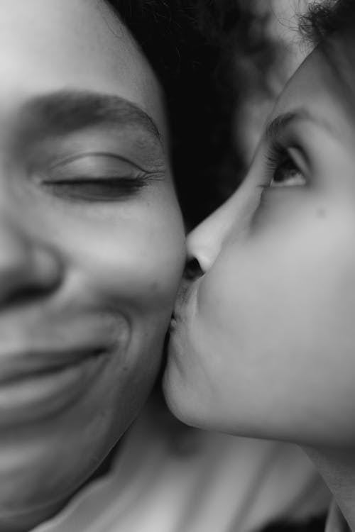 Grayscale Photo of a Young Girl Kissing a Woman