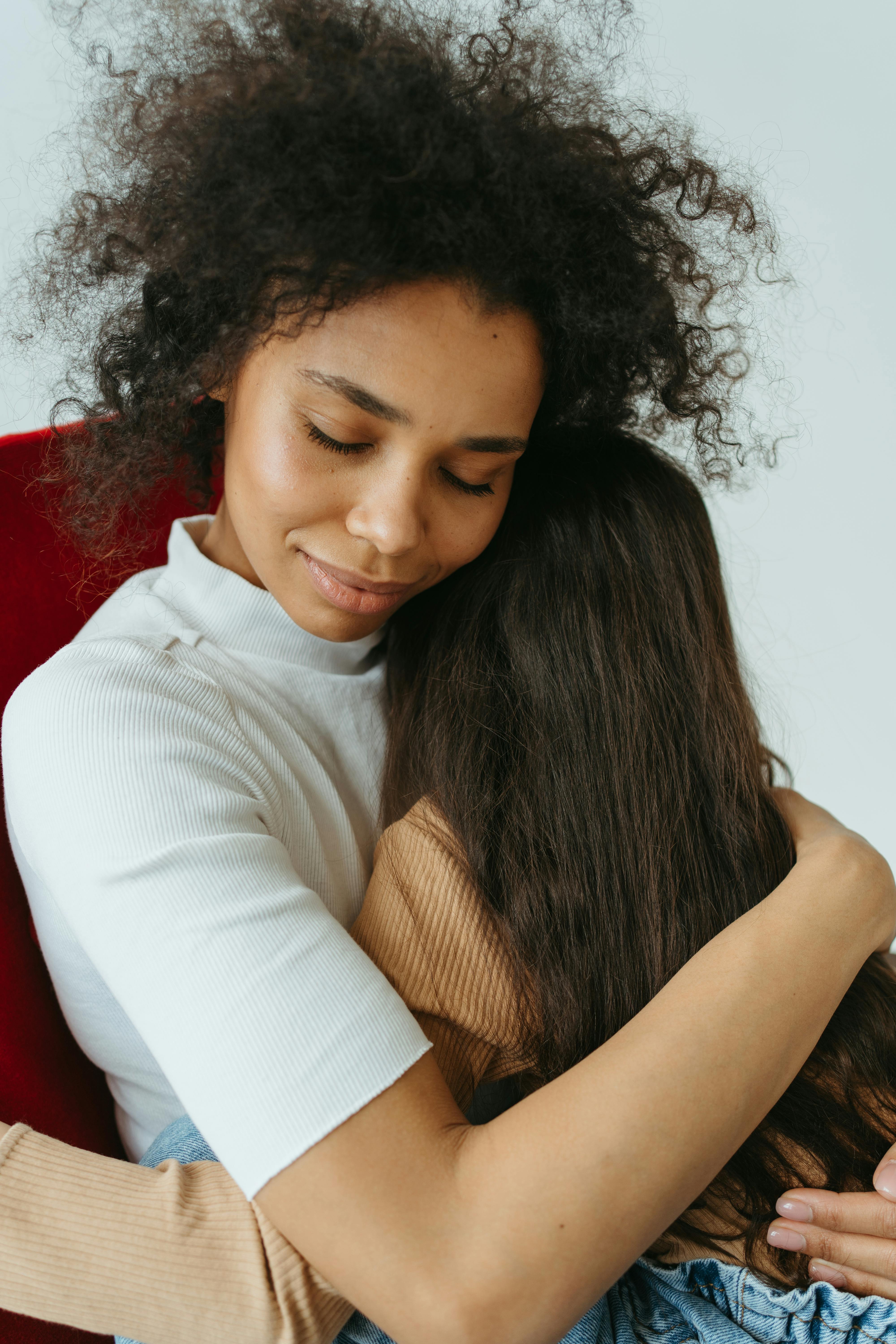 A black woman with afro hair lovingly embracing her child indoors, showcasing warmth and affection.