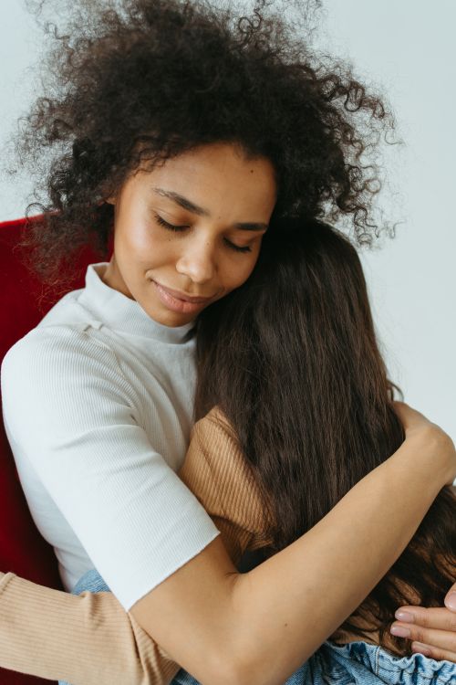 Free A black woman with afro hair lovingly embracing her child indoors, showcasing warmth and affection. Stock Photo