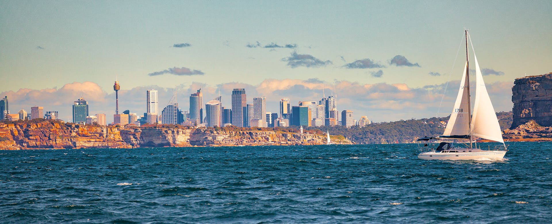 A scenic view of a sailboat near Sydney Harbour with the city skyline in the background.