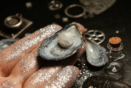 From above of female hand showing sparkling pearl in mollusc seashell on hand on blurred background