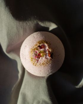 Top view pink fragrant bath bomb in shape of ball placed on dark cloth