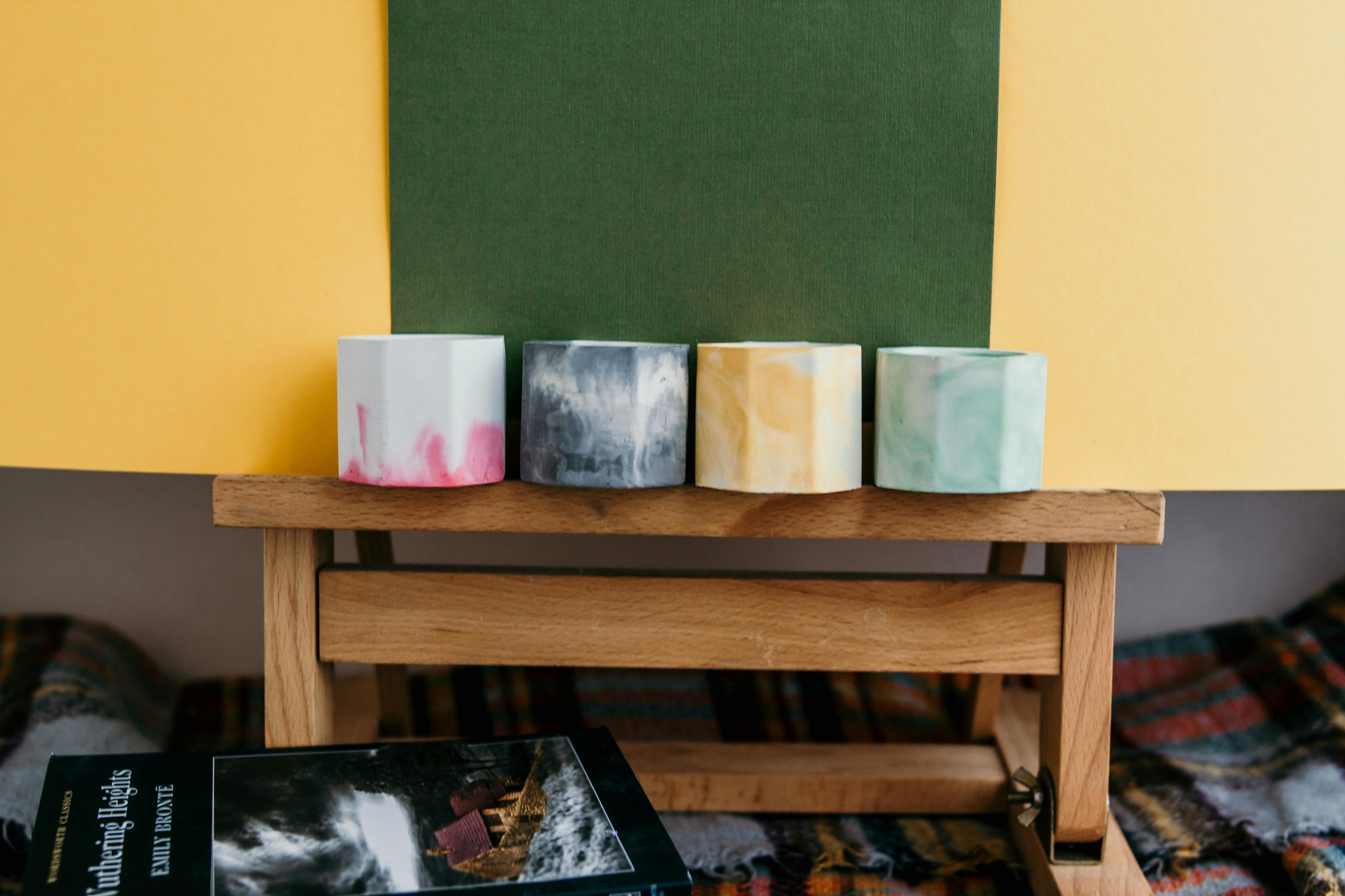 A set of multicolored handmade candle holders arranged on a wooden stand indoors.