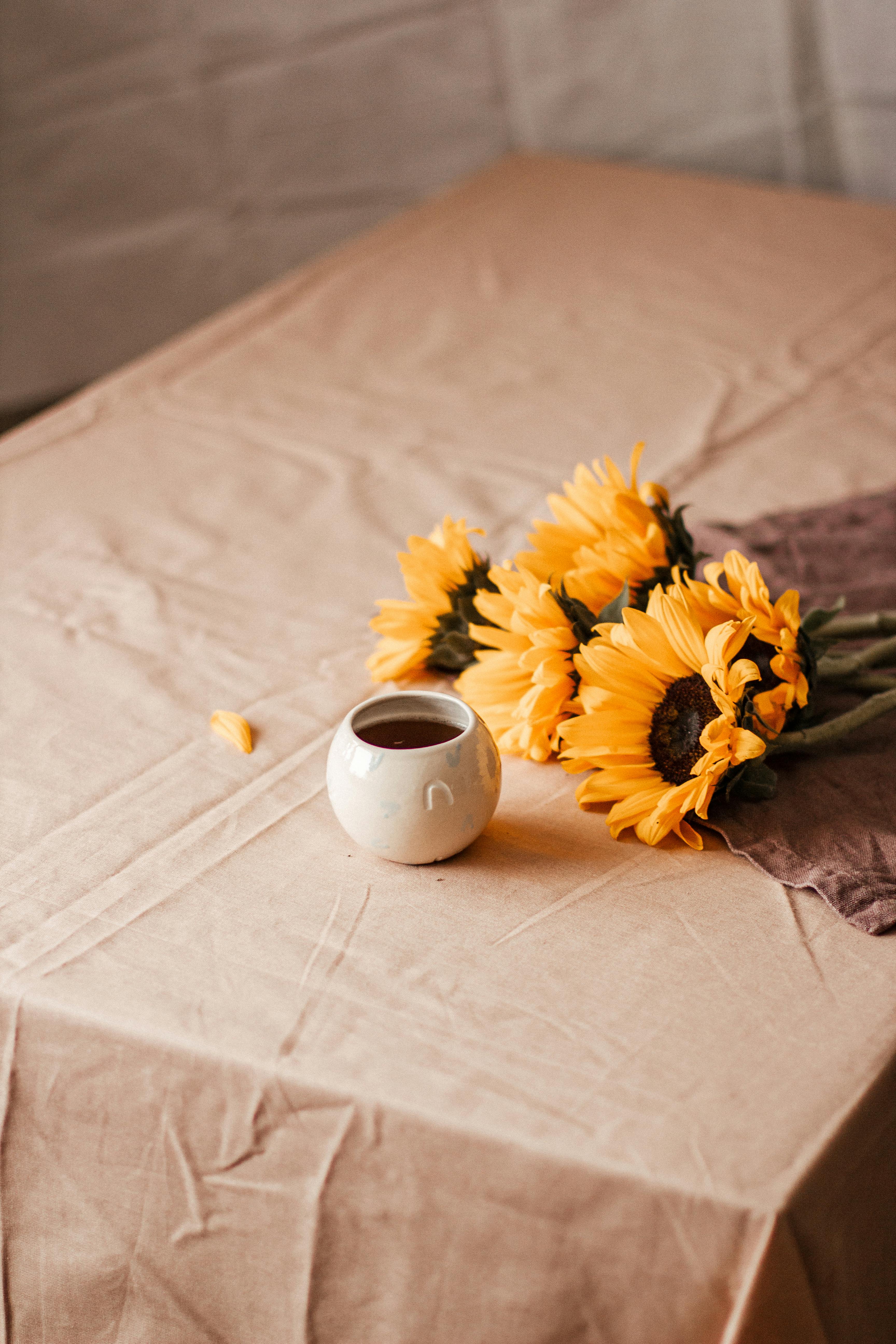 High angle of aromatic coffee placed near bunch of blossoming flowers in crumpled tablecloth