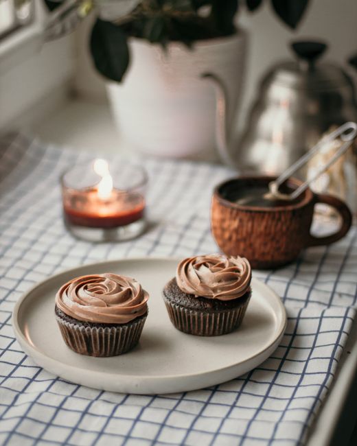 High angle of delicious homemade cupcakes topped with cream served on windowsill near burning candle and kettle