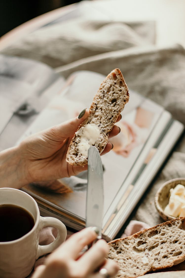 Woman Spreading Butter On Bread For Breakfast With Coffee