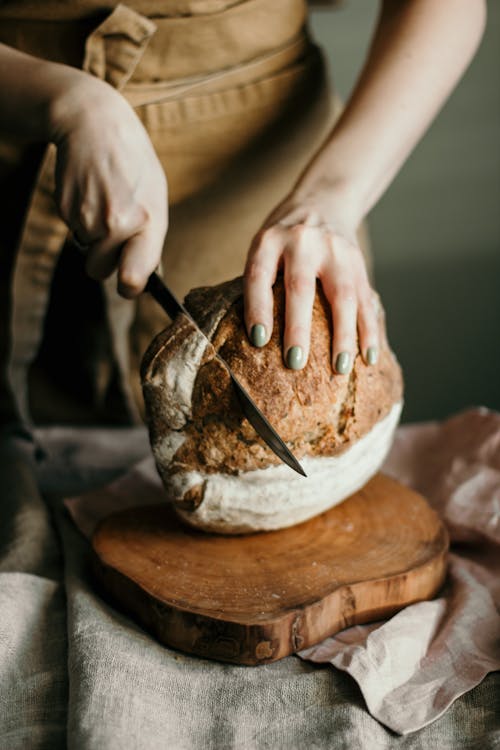 Free Woman cutting sourdough bread on wooden cutting board Stock Photo