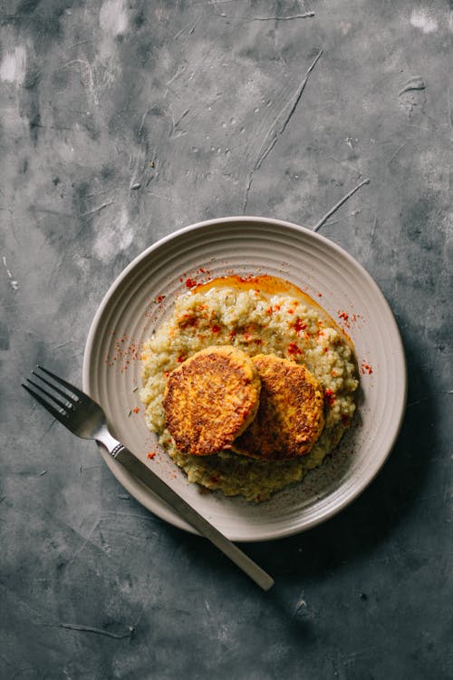 Top view of porridge with pepper served with vegetarian cutlets on plate with fork on table