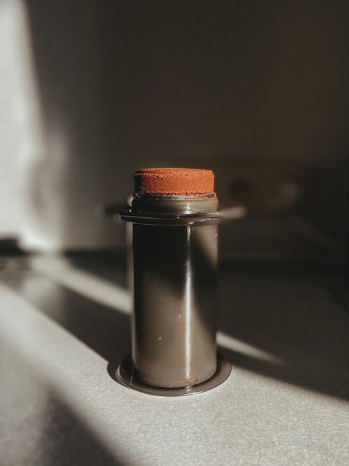 Ground coffee beans in cylindrical aeropress placed on table in kitchen at sunlight
