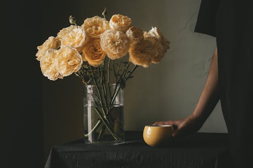 Free Crop person with coffee near bouquet of flowers Stock Photo