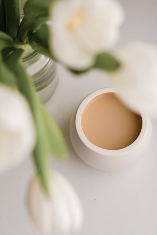 Free Top view of bouquet of white flowers in glass jar near mug of hot coffee with milk on white background Stock Photo