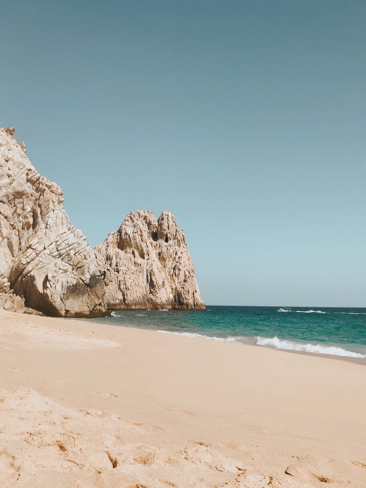 Beautiful view of a sandy beach and rugged rock formations at Cabo San Lucas, Mexico under a clear blue sky.
