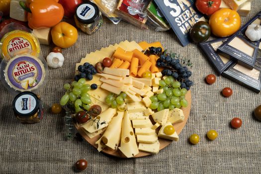 Aesthetic cheese platter with fresh grapes and vegetables on burlap background, ready for serving.