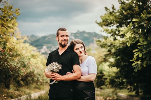 Free A loving couple embracing outdoors with a bouquet, surrounded by lush greenery. Stock Photo