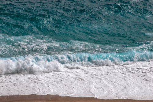 Free Captivating view of turquoise ocean waves crashing onto a golden sandy beach, showcasing nature's beauty. Stock Photo