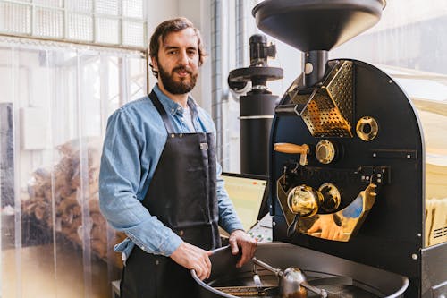 A Bearded Man Standing Near a Coffee Roaster