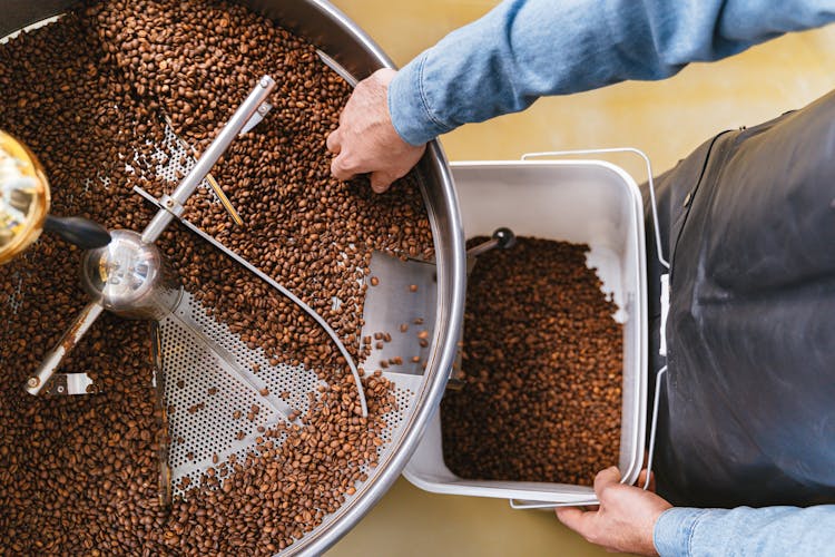 A Person Holding A Bucket While Getting Coffee Beans From The Machine