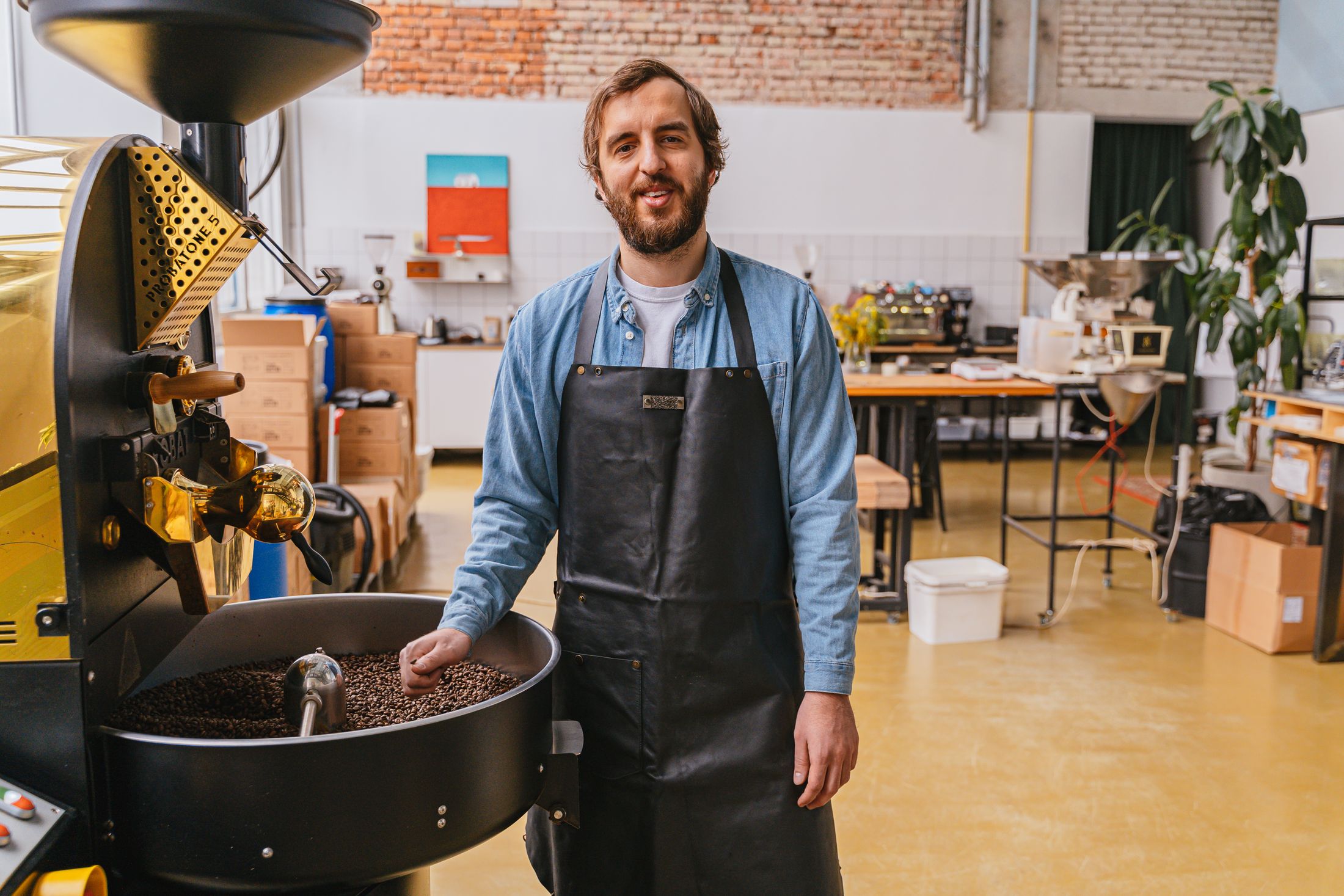 Professional coffee roaster at work beside a roasting machine