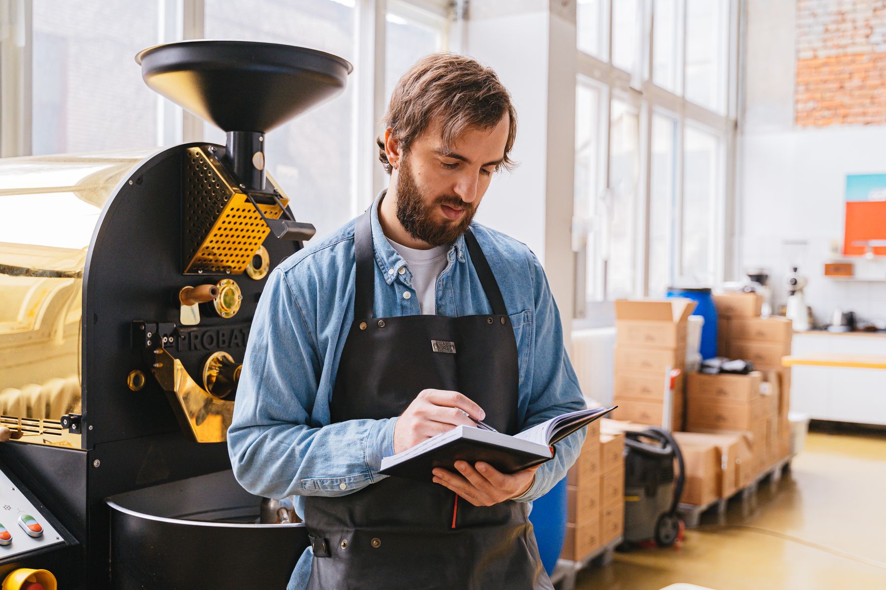 Kaffeeröster in Schürze macht sich neben der Röstmaschine Notizen